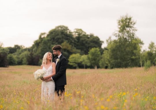 A couple called Patricia and Daniel who go married at Galgorm, standing in a field in wedding attire posing. 