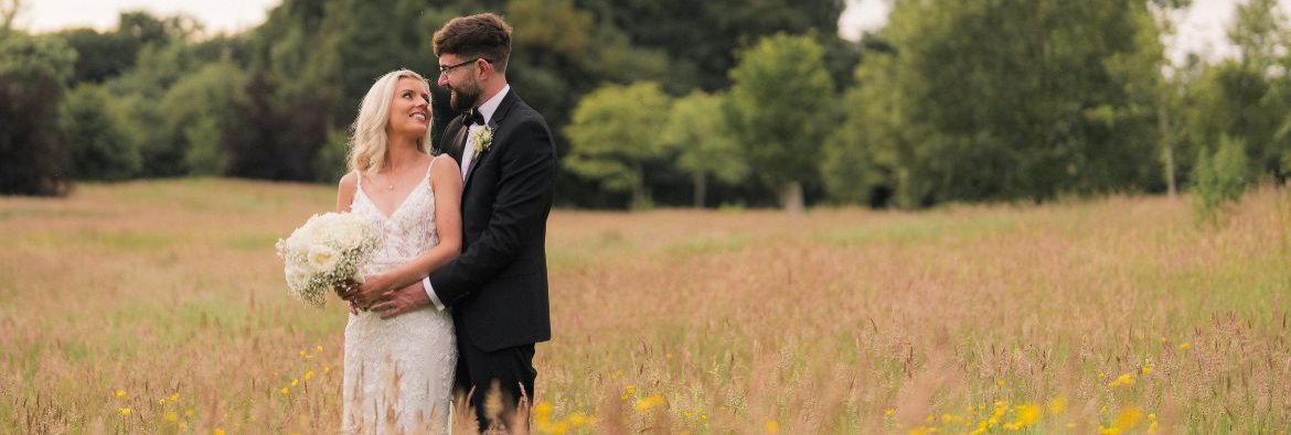 A couple called Patricia and Daniel who go married at Galgorm, standing in a field in wedding attire posing. 